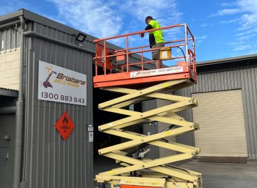 A worker in high-vis clothing standing on an elevated scissor lift performing maintenance on a building exterior