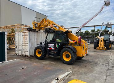 A JCB telehandler lifting equipment onto a shipping container at a construction site