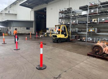 A worker operating a yellow forklift truck near a warehouse entrance, manoeuvring through safety cones - Licence to operate a forklift truck