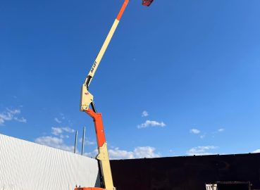 A fully extended boom lift reaching high into the sky with a worker in the platform