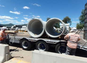 Securing Concrete Pipes for Transport – Workers in high-visibility clothing securing large concrete pipes on a flatbed trailer at an industrial site