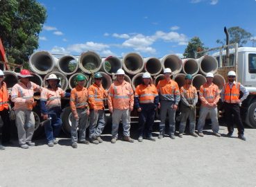 A group of workers in high-visibility clothing standing in front of a truck loaded with concrete pipes, showcasing teamwork and logistics in the industry