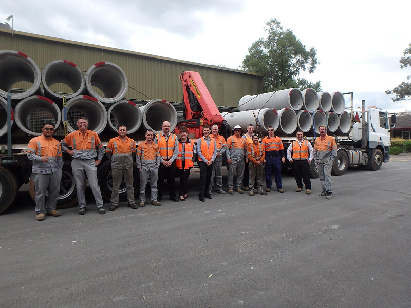 A group of workers in high-visibility clothing standing in front of a truck loaded with concrete pipes, showcasing teamwork and logistics in the industry
