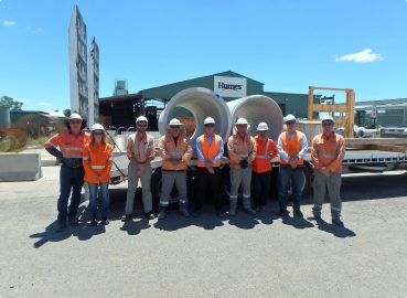 A group of workers in high-visibility clothing standing in front of a truck loaded with concrete pipes, showcasing teamwork and logistics in the industry
