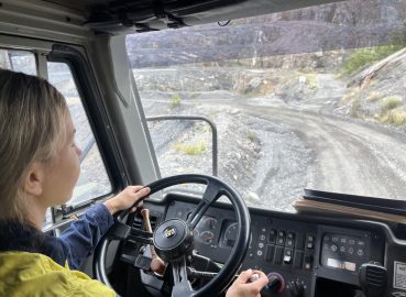 A woman operating a large mining truck on a dirt road, demonstrating hands-on training in heavy machinery operation
