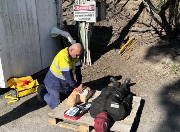 A worker in high-vis clothing performing CPR on a mannequin during a first aid training session, reinforcing safety and emergency preparedness