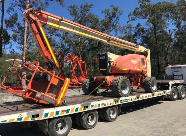 A large orange boom lift secured on a flatbed trailer, prepared for transport