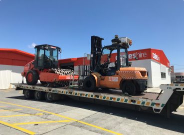 A low-loader trailer carrying a forklift and a road roller, representing machinery transport in the civil and mining sectors