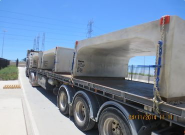 Large pre-cast concrete bridge sections secured on a flatbed truck, ready for transport
